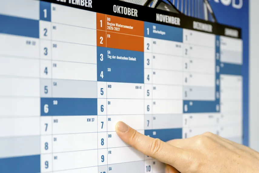 Wandkalender in den Farben des Ruhr Innovation Lab mit Hand, die auf 7. Oktober zeigt